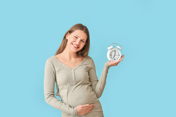 Canvas Print - Pregnant young woman with clock on color background