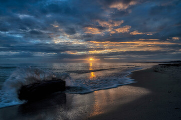 Alba sul mare con cielo nuvoloso e riflesso del sole sull'acqua e sulla spiaggia.