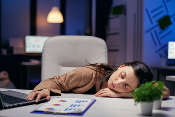 Poster - Tired businesswoman resting head on desk holding hand on laptop. Employee falling asleep while working late at night alone in the office for important company project.