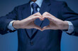 Handsome man show heart symbol, love icon for Business lover, I love my job, take care service concept. Smart Businessman wear blue suit shirt tie making heart shape by his hand on blue background.