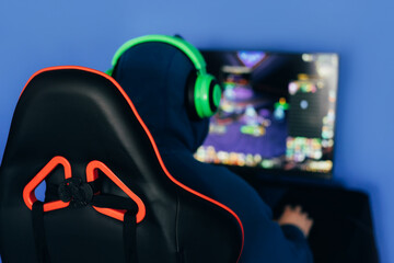 Wall Mural - The gamer sits on a gaming chair and plays computer games. The player has green headphones on his head.