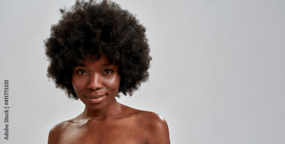 Beauty portrait of attractive african american young woman with afro hair and perfect smooth glowing skin smiling at camera while posing isolated over gray background - obrazy, fototapety, plakaty 