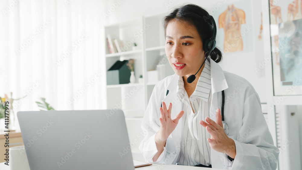 Young Asia lady doctor in white medical uniform with stethoscope using computer laptop talking video conference call with patient at desk in health clinic or hospital. Consulting and therapy concept. - obrazy, fototapety, plakaty 
