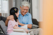 © tirachard - Asian grandfather relax at home. Senior Chinese, grandpa happy relax with young granddaughter girl enjoy read books and do homework together in living room concept.