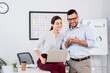 © LIGHTFIELD STUDIOS - cheerful business people looking at smartphone near laptop and paper cup on desk