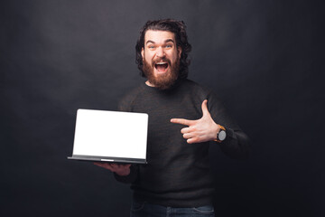 Wall Mural - Photo of amazed bearded man screaming and pointing at blank screen on laptop.