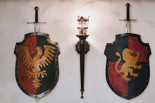 Shields, Swords And A Torch-shaped Wall Lamp. Medieval Concept And Knightly Elements. Decorative Eagle And Lion.