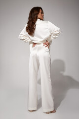 Sexy brunette woman luxury lifestyle bright makeup wear natural organic white silk suit pants blouse and high heels perfect body shape fashion model style for meeting party or romantic date studio.