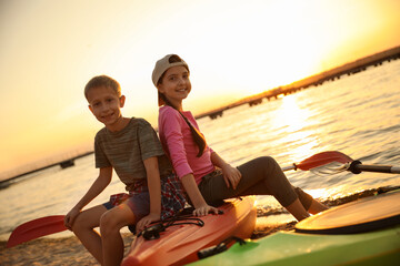 Sticker - Happy children sitting on kayak near river at sunset. Summer camp