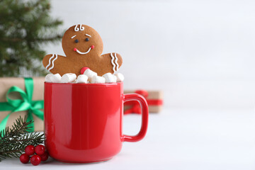 Wall Mural - Gingerbread man in red cup with marshmallows on white table, space for text