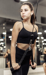 Wall Mural - Young fit woman trains misci triceps in crossover exercise machine with ropes. Girl trains arms in modern gym