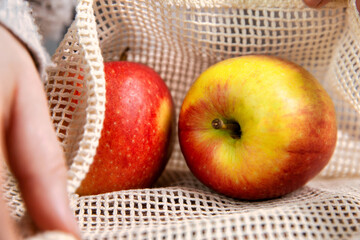 Female hand with environmentally friendly net bag for shopping groceries with Fresh fruit, Apples and oranges, eco friendly net on wooden table