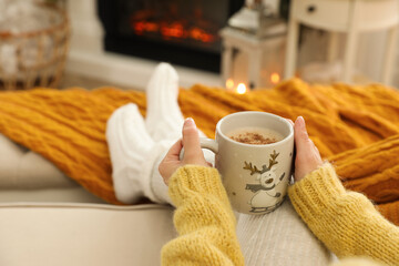 Canvas Print - Woman with cup of hot drink resting on sofa near fireplace in living room, closeup