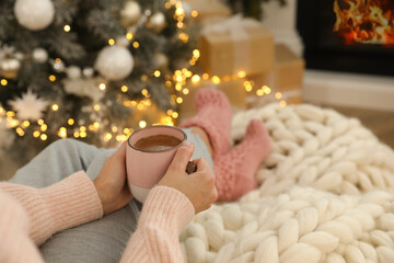 Canvas Print - Woman with cup of hot drink resting near fireplace  in living room decorated for Christmas, closeup