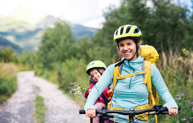 Wall Mural - mother with small daughter cycling outdoors in summer nature, looking at camera.