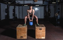 Young Sweaty Muscular Fit Girl With Big Muscles And Strong Legs Doing Deep Squat And Dip On Two Wooden Jump Boxes With Heavy Kettlebell For Hardcore Strength Workout Training In The Gym 