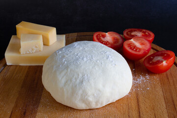 Pizza dough with tomatoes, parmesan on wooden board on black background. Pizza Margherita. Pizza ingredients