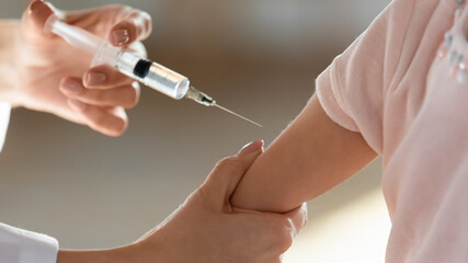 Wall Mural - Crop close up of female nurse hold syringe make injection give vaccine to small child patient at checkup in hospital. Woman doctor vaccinate prick arm of little kid in clinic. Vaccination concept.