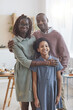 © Seventyfour - Vertical portrait of happy African-American family looking at camera while posing indoors in cozy home interior with dinner table in background