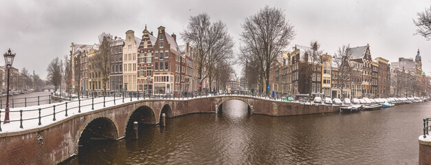 Winter snow view of Dutch canal and old houses in the historic city of Amsterdam, the Netherlands