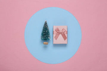 Wall Mural - Mini Christmas tree and gift box on a blue-pink round background. Minimalism