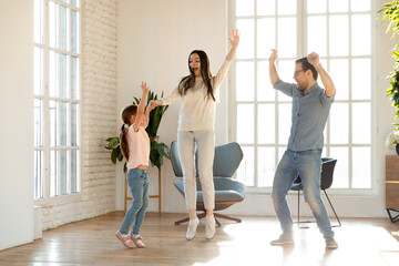 Sticker - Overjoyed young Caucasian family renters with little 7s daughter have fun dancing together in cozy living room on weekend. Happy mom and dad enjoy family time with small girl child moving to new home.