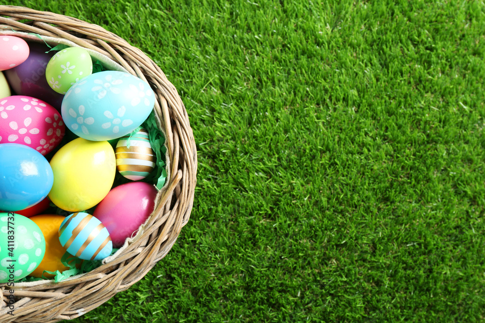 Wicker basket with Easter eggs on green grass, top view. Space for text - obrazy, fototapety, plakaty 