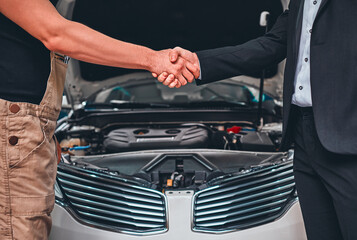 Close up view cropped shot, of a side profile view of businessman in a classy suit shaking arm of a mechanic, near the hood of his property.