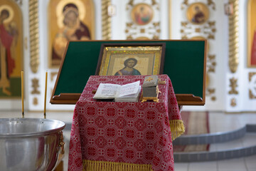 Wall Mural - The interior of a Christian church. Prayer table covered with patterned red cloth. Bible, casket, icon and blurred iconostasis in the background.