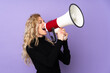 © luismolinero - Young blonde woman isolated on purple background shouting through a megaphone