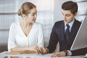 Business people discussing something while sitting in sunny office. Focus at businesswoman while talking to her male colleague