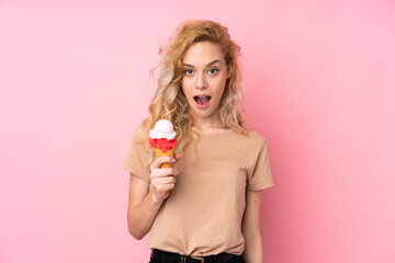 Canvas Print - Young blonde woman holding a cornet ice cream isolated on pink background with surprise and shocked facial expression