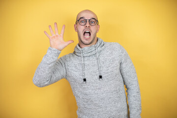 Wall Mural - Young bald man wearing glasses over yellow background showing and pointing up with fingers number five while smiling confident and happy