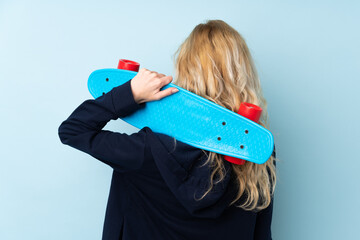 Wall Mural - Young blonde woman isolated on blue background with a skate in back position