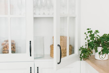 
Opened Door Of White Glass Cabinet With Clean Dishes And Decor. Scandinavian Style Kitchen Interior. Organization Of Storage In Kitchen. Selective Focus.