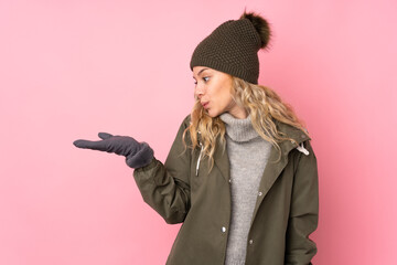 Poster - Young girl with winter hat isolated on pink background holding copyspace imaginary on the palm