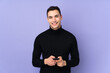 © luismolinero - Young caucasian handsome man with turtleneck sweater isolated on purple background sending a message with the mobile