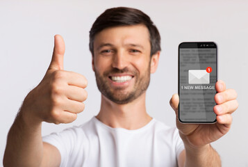 Poster - Man Showing Smartphone With New Message Gesturing Thumbs-Up, Gray Background