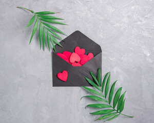 Wall Mural - Red wooden figures of hearts are in a black envelope on a gray concrete background. There are green leaves nearby. Floral layout for valentine's day, mother's day. Flat lay. Top view.