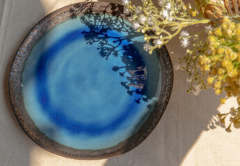 Wall Mural - Ceramic plate and flowers on white textured table cloth. Top view, Selective focus.