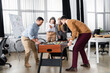 © LIGHTFIELD STUDIOS - Cheerful multiethnic businessmen playing table soccer near smiling businesswomen in office