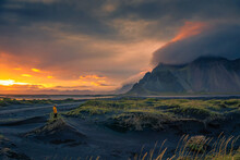 Tourist stands on a sand dune at Vestrahorn mountain in Iceland at sunset
