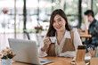 © amnaj - Young Beautiful smiling Asian business woman holding a coffee and laptop Placed at the wooden table at the office