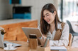 © amnaj - Asian businesswoman smiling looking at a tablet at her desk at the office.
