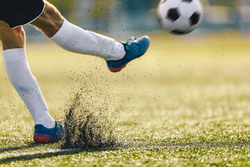 Wall Mural - Adult Soccer Player Kicking Ball On Sunny Day on Artificial Football Pitch. Closeup Image of Footballer Legs and Sports Ball in Motion