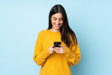young caucasian woman isolated on blue background sending a message with the mobile