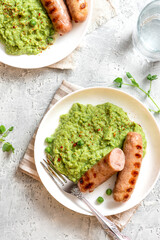 Wall Mural - Pea mash and grilled sausages in a white ceramic plate on a gray concrete table top view. Tasty balanced lunch or dinner.