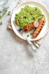 Wall Mural - Pea mash and grilled sausages in a white ceramic plate on a gray concrete table top view. Tasty balanced lunch or dinner.