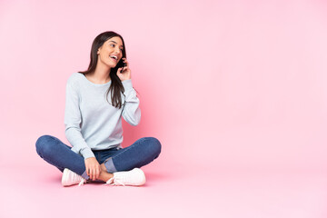 Wall Mural - Young caucasian woman isolated on pink background keeping a conversation with the mobile phone