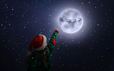 Wall Mural - Cute little girl looking at Santa Claus with reindeers in sky on full moon night. Christmas holiday